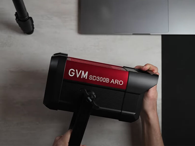 GVM SD300B-AIO: Your All-in-One 300W LED Video Light 6 Hands holding the GVM SD300B-AIO 300W LED video light, perfectly showcasing its compact, all-in-one design and built-in handle. This integrated system simplifies setup, making it an ideal portable 300W LED video light for solo creators and small crews.