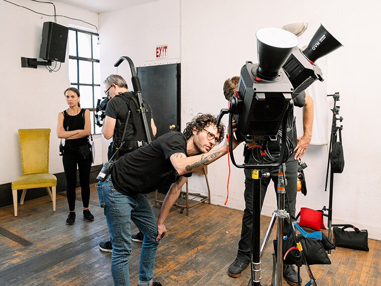 Mastering Your Light: A Deep Dive into Video Lighting Parameters 1 A busy professional video production set with crew adjusting and moving high-end video lighting equipment and camera gear, showcasing a typical studio setup.