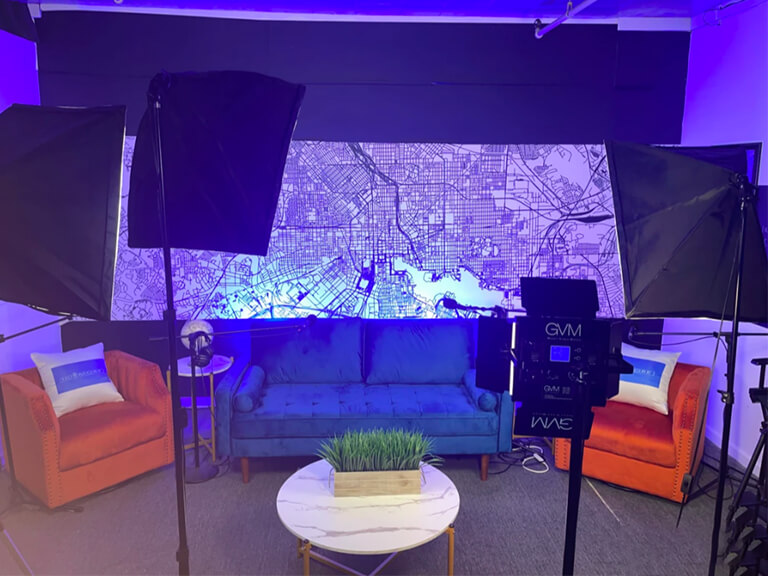 Podcast Background Lighting Ideas: Add Ambiance & Depth to Your Studio 3 A modern podcast studio setup with a couch, table, and dynamic RGB background lighting in blue and purple tones, illustrating a futuristic ambiance.