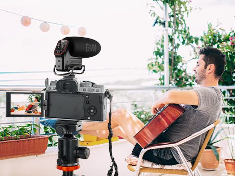 Musician recording acoustic guitar outdoors with GVM QX-6 on-camera microphone mounted on a DSLR.