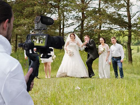 Videographer filming an outdoor wedding party using a gimbal stabilizer and GVM QX-6 shotgun microphone mounted on a DSLR camera. (