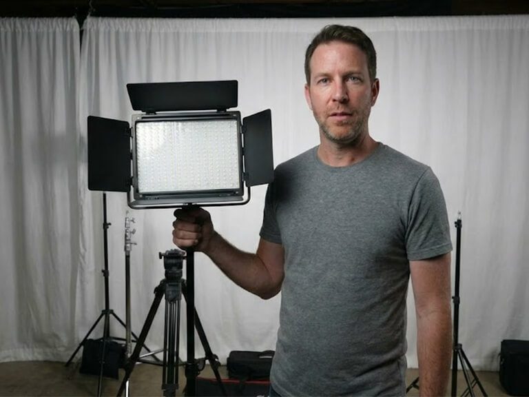 Content creator adjusting a large GVM LED video light panel with barndoors on a stand during a studio lighting setup.