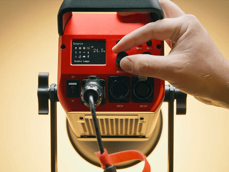 Indoor Photography Lighting: 16 Tips to Simulate Natural Light 9 A hand adjusting the intensity knob on a red professional Photography Lighting unit, showing a digital display set to 24.5% to manage light fall-off and create a natural gradient.