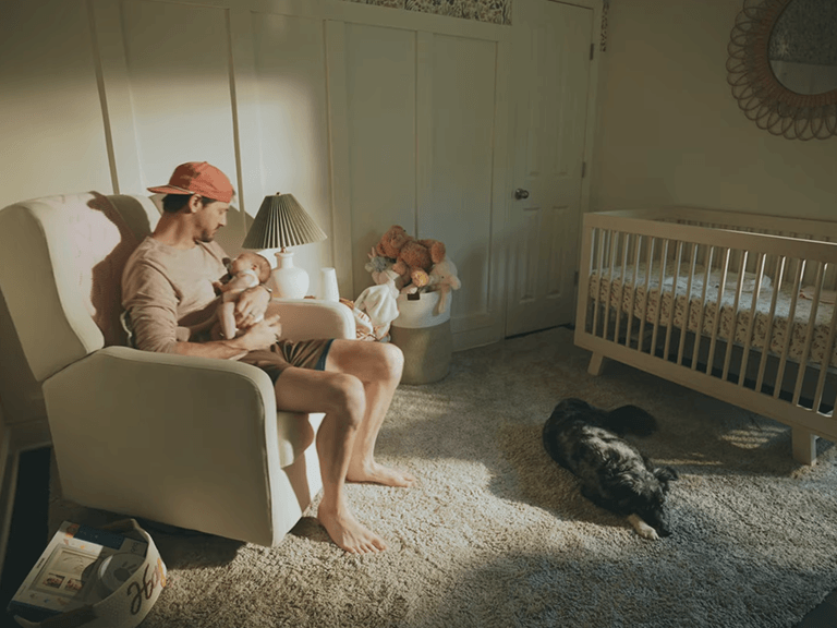 Indoor Photography Lighting: 16 Tips to Simulate Natural Light 11 A man holding a baby in a bright nursery with a dog on the rug, illustrating a Photography Lighting setup designed to mimic soft, natural morning sunlight.