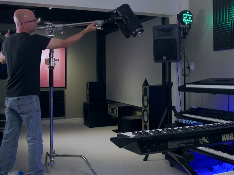 Wind, Sand, and Uneven Concrete: How to Choose a Light Stand for Location Shoots 2 Professional videographer mounting a high-power LED video light onto a heavy-duty stainless steel C-stand with a boom arm.